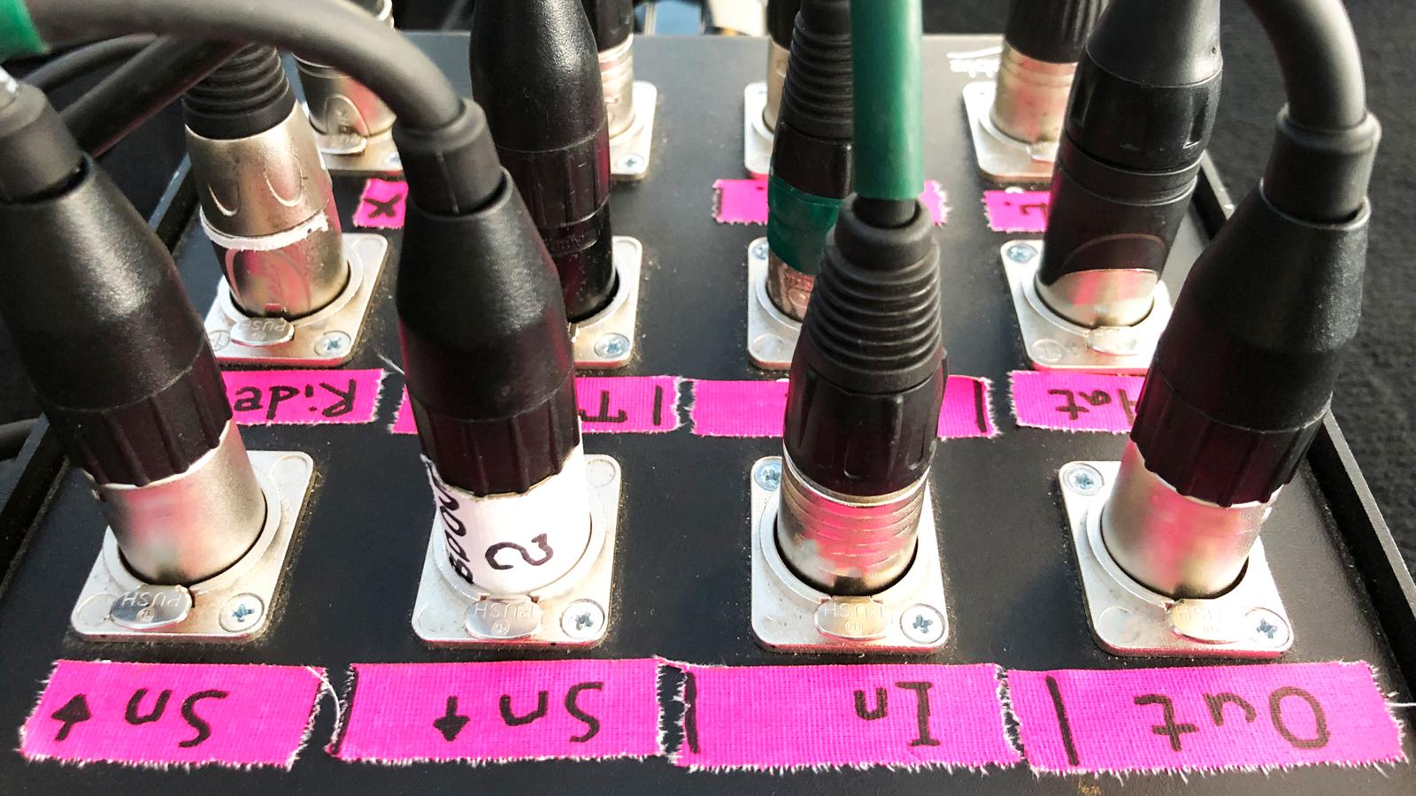 XLR cables plugged into a stage box with taped channel labels